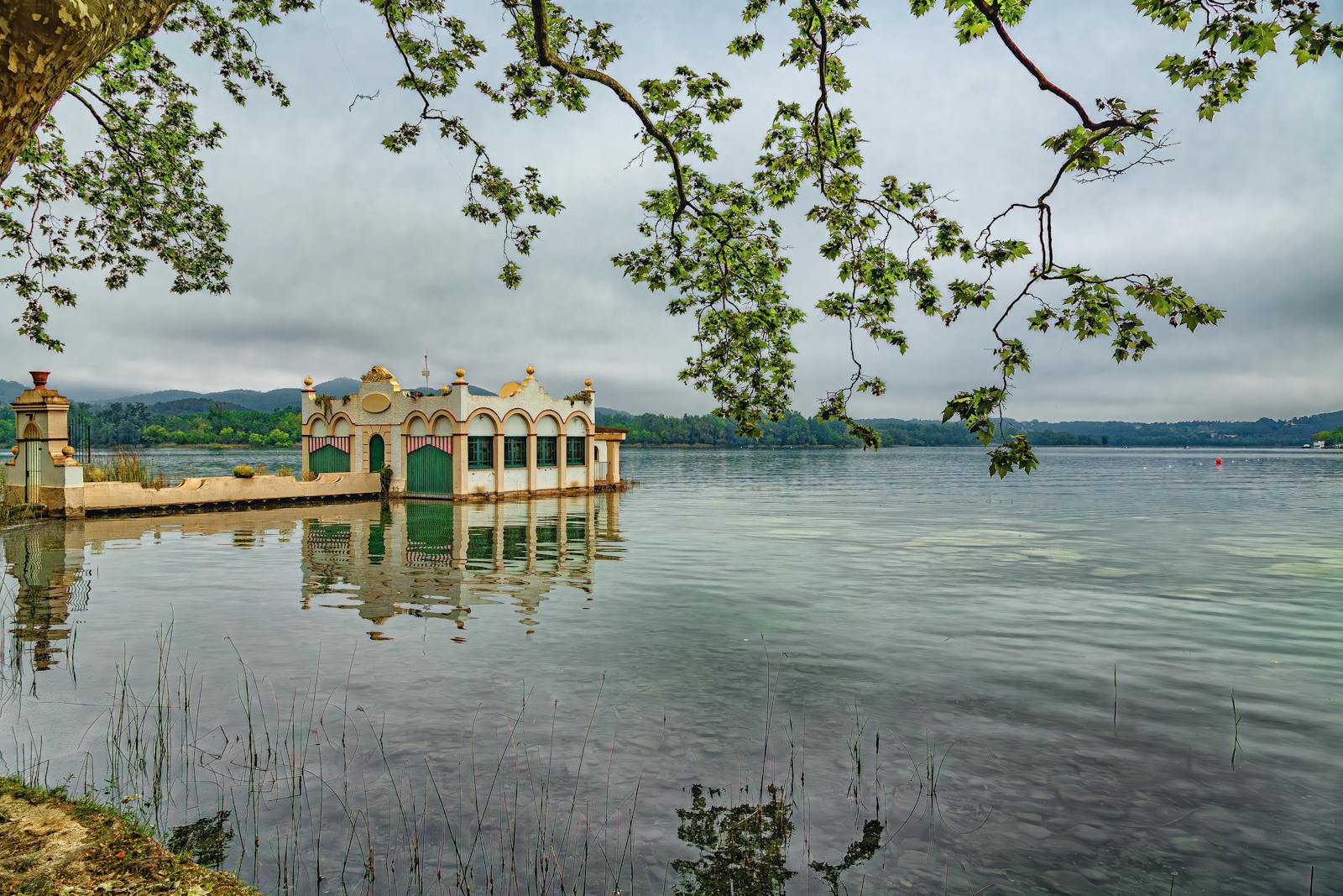 Serene lake view with reflections and unique architectural structure in Cadaqués, Spain.